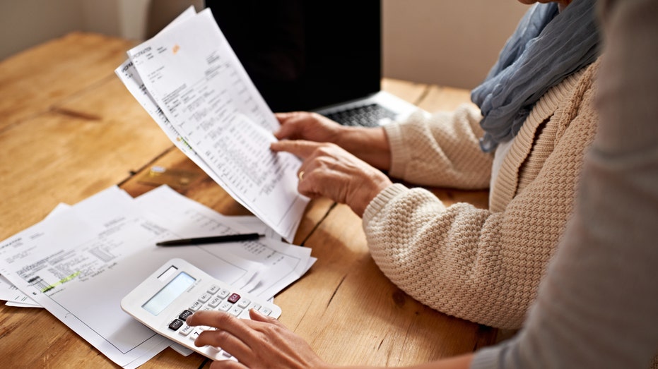 A person using a calculator and another person pointing at a sheet of paper